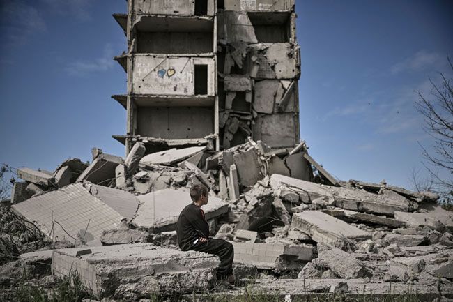 ウクライナ東部ドンバス地方で、破壊された建物の前に座る少年＝2022年5月25日【ＡＦＰ時事】　ウクライナの国営通信は…