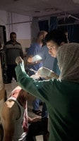 １２日、パレスチナ自治区ガザの病院で、停電の中、携帯電話のライトを頼りに治療に当たる医師ら（ＳＮＳの映像より）（ロイター時事）